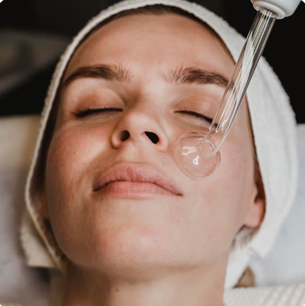 paciente mujer con turbante en cabeza recibiendo tratamiento facial con aparato de estetica